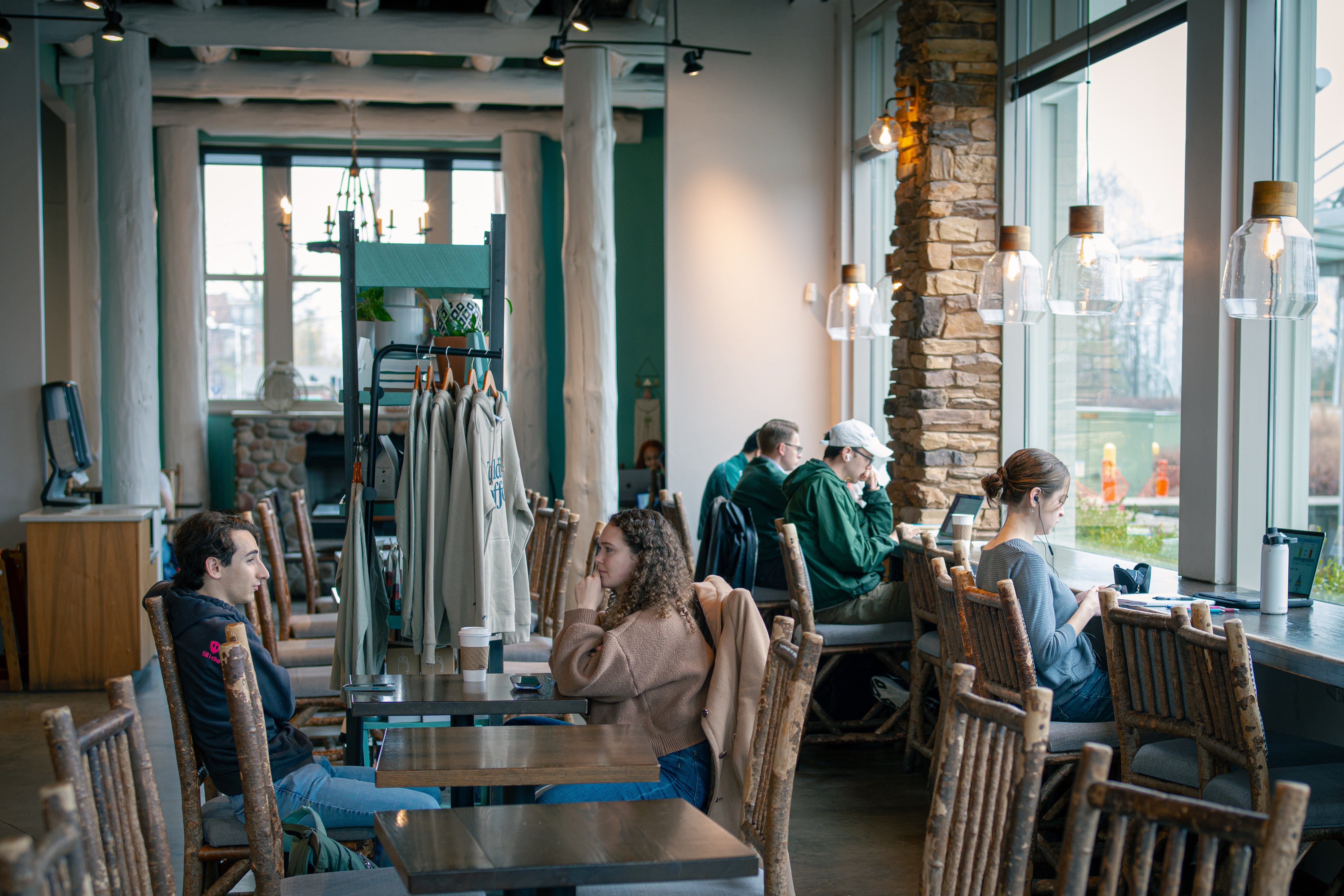 People sitting at tables in a cozy cafe with large windows and wooden chairs.