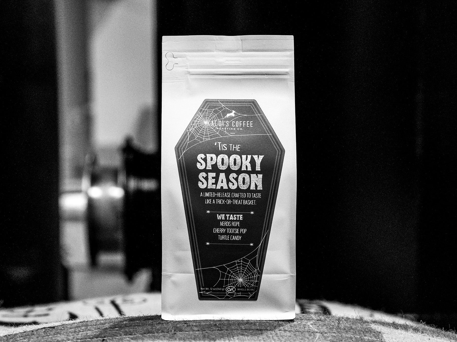 Coffee package labeled 'Tis the Spooky Season' on a wooden surface with a blurred background.