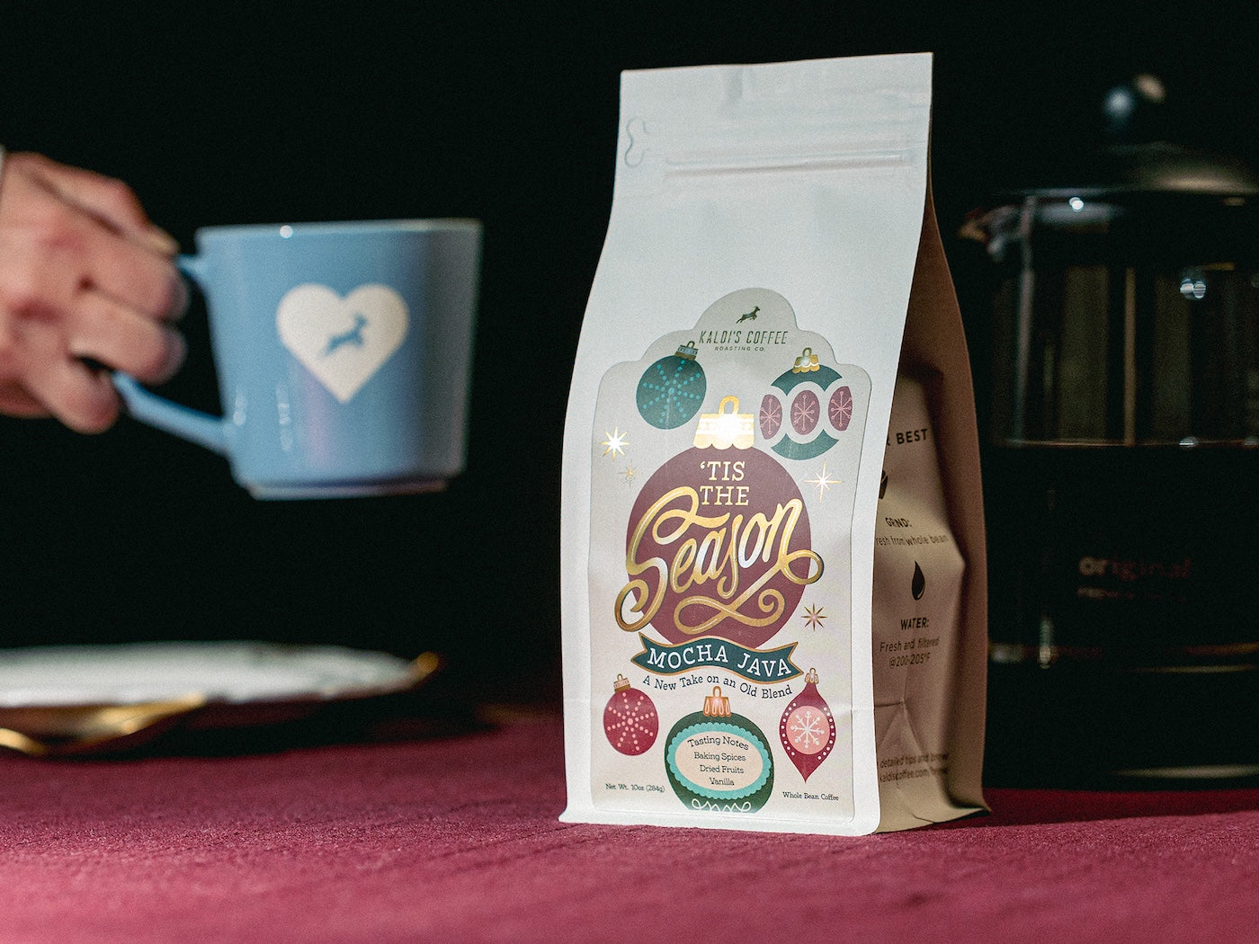 Tis the Season coffee blend with and holding a blue mug