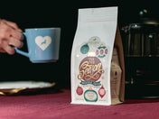 Tis the Season coffee blend with and holding a blue mug