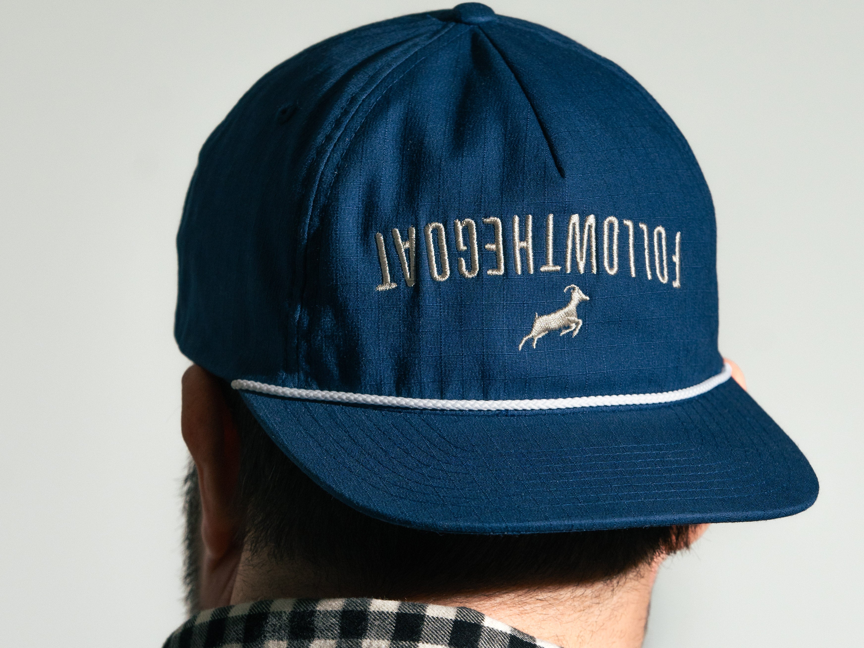 Blue cap with 'FOLLOWTHEGOAT' text and logo on a plain background
