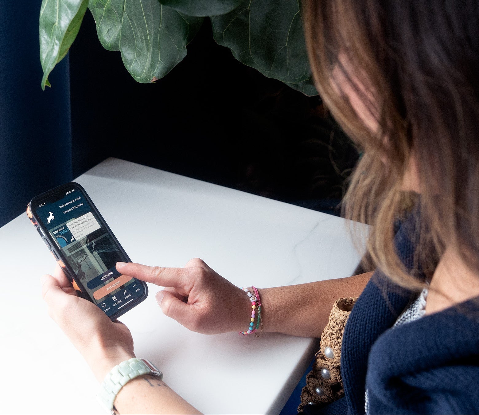 Person using a smartphone at a table with a plant in the background