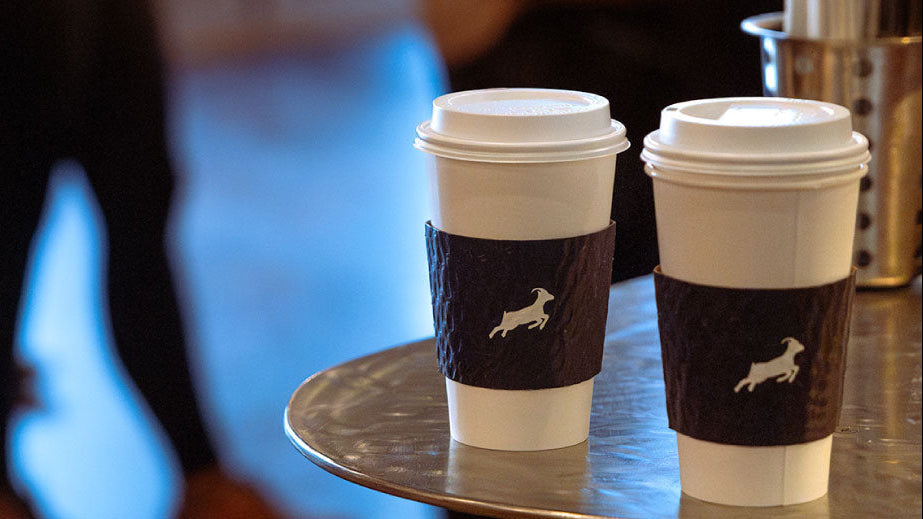 Two coffee cups with brown sleeves on a table with a blurred background