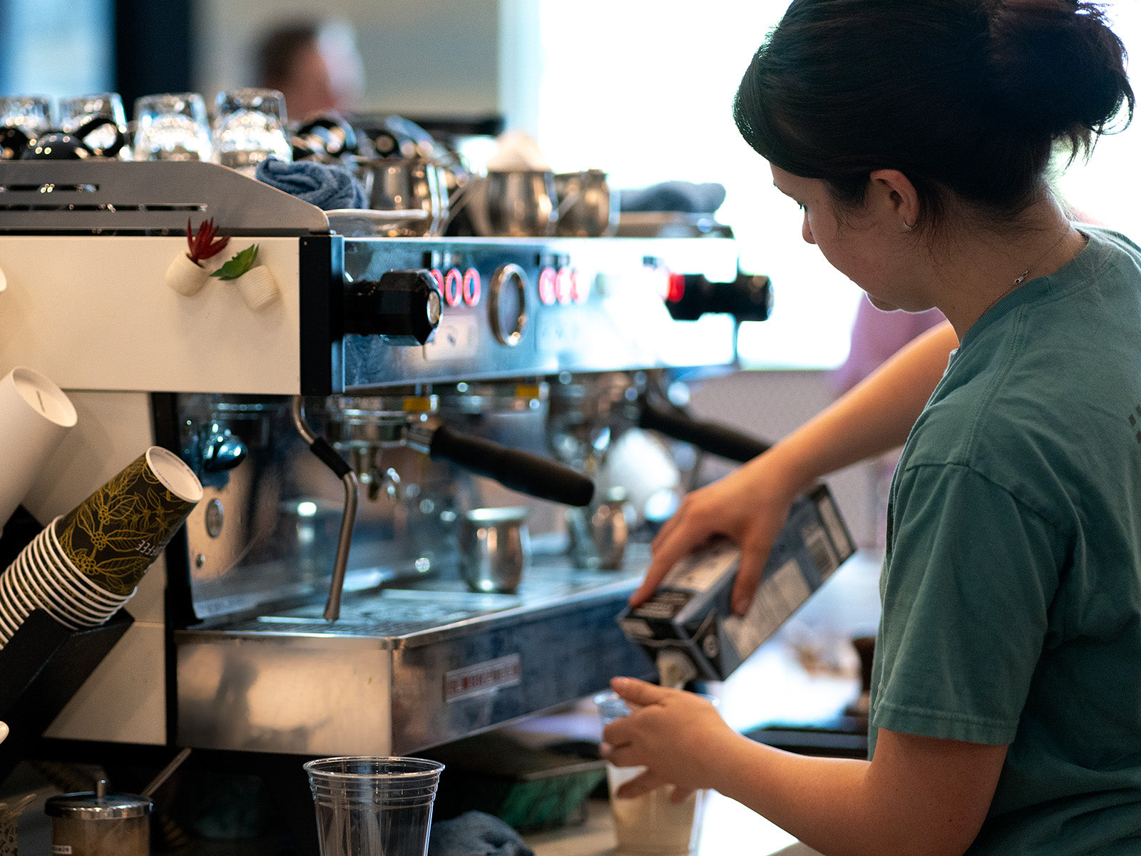 Person working behind a coffee machine in a cafe setting