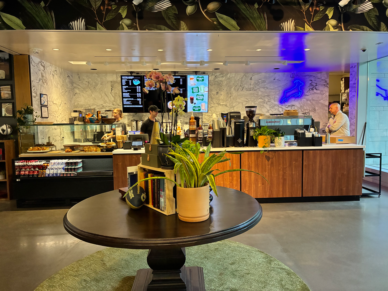 Cafe interior with wallpaper and console table. Bakery case displays drinks and bakery.