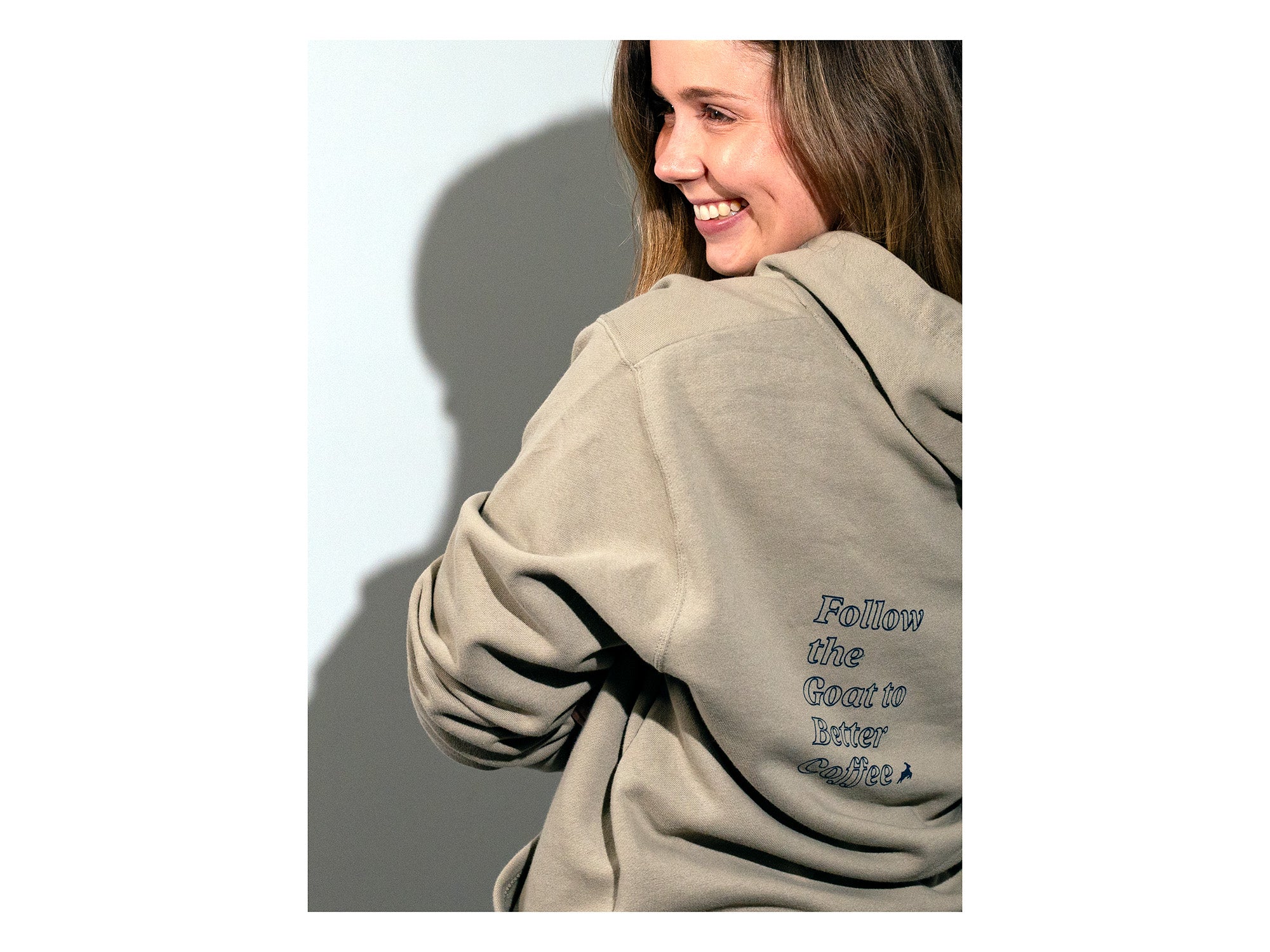 Shoulder shot of a model wearing a hooded sweatshirt that displays "Follow the Goat to Better Coffee"